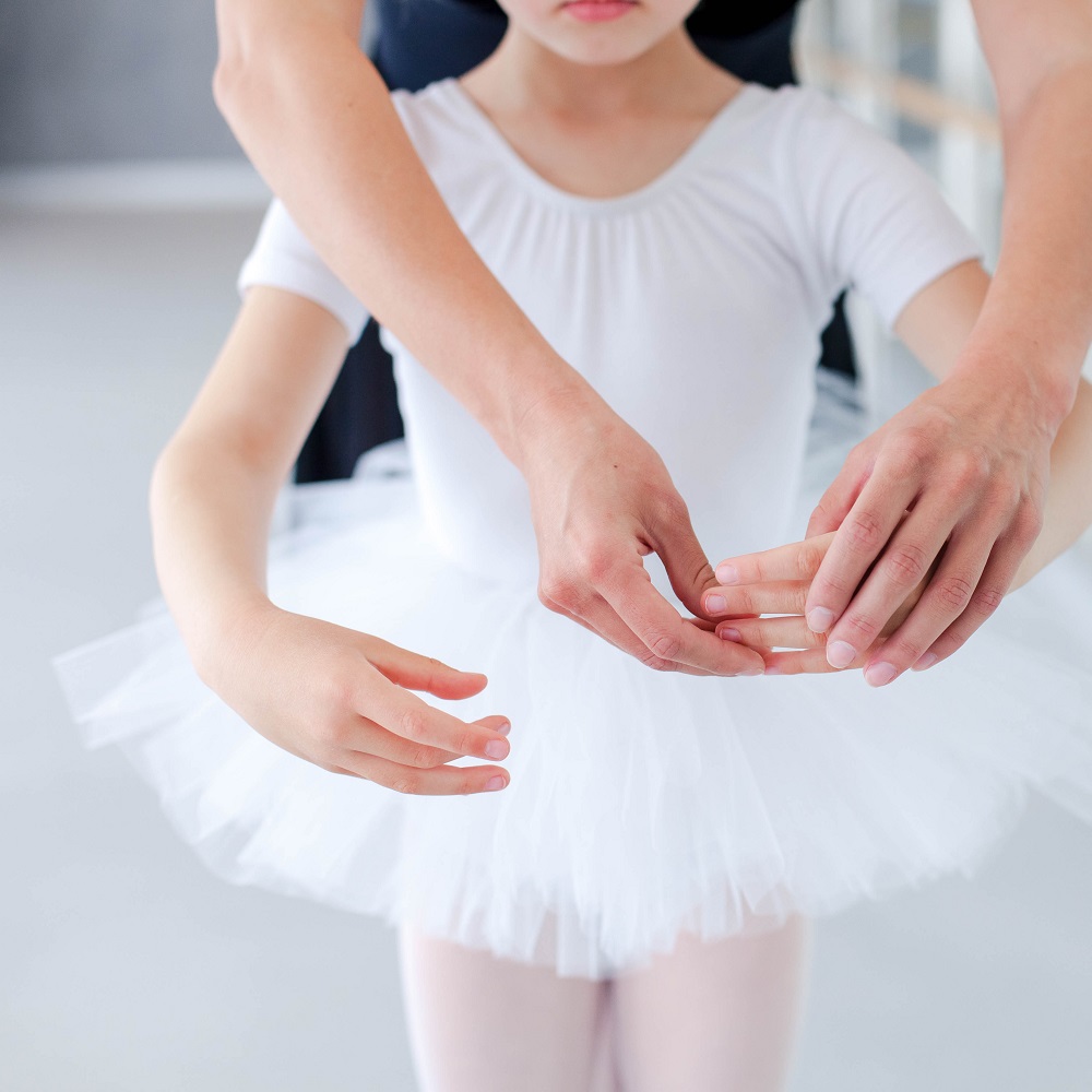 Ballet teacher and little ballerina in classical dancing school. Female dance trainer corrects hands of kid. Practicing for children. Close up.
